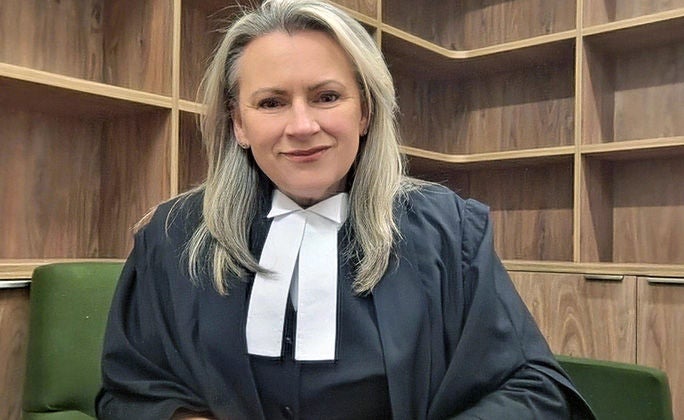 Jodie, an Associate for a County Court Judge, sits in an office on a green chair, with cabinets and shelves in the background.