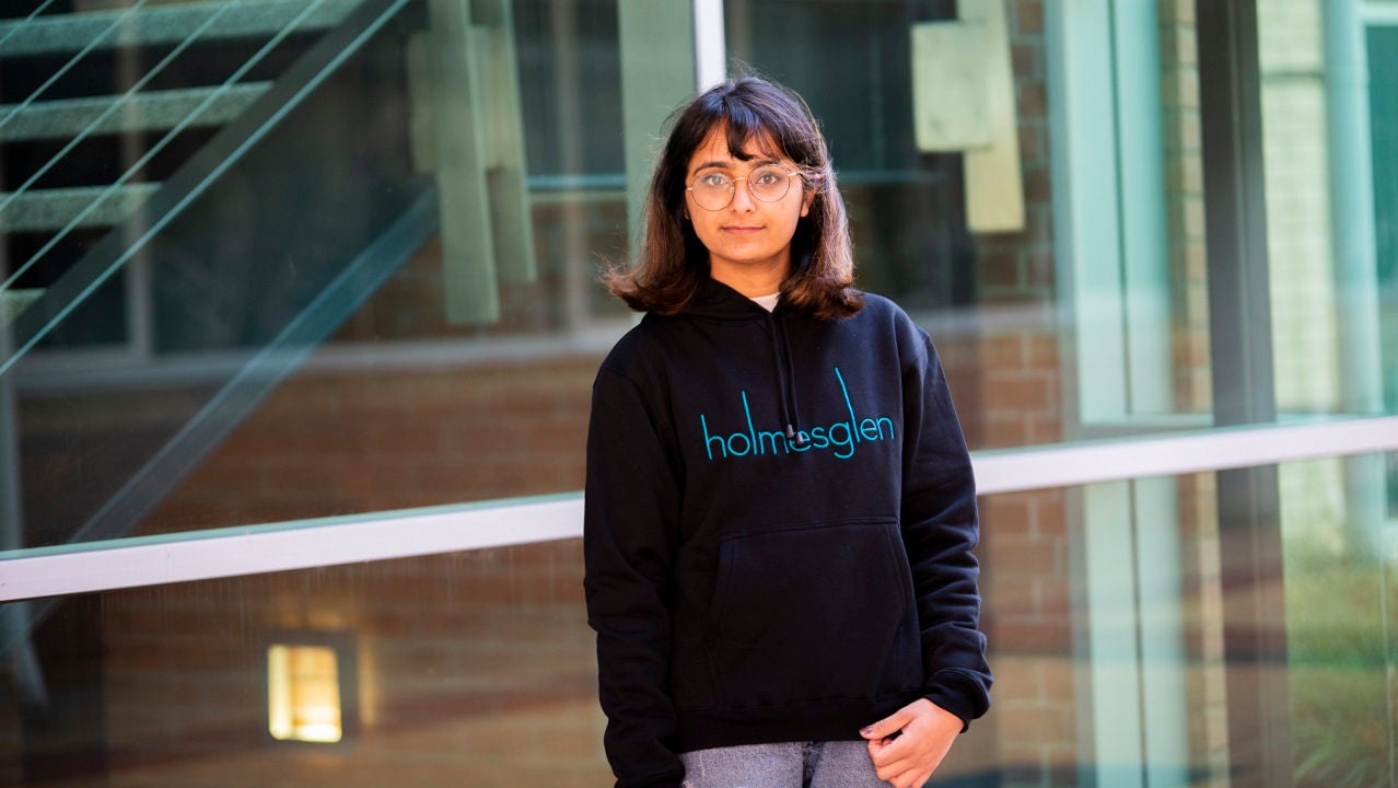 Holmesglen student, Rimpal, stands in front of building, wearing a Holmesglen hoodie.
