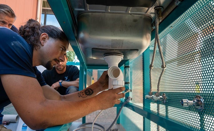 A plumbing apprentice installs a sink pipe while in a plumbing training pod.