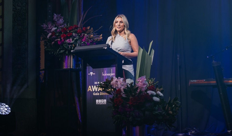 Female student stands on stage behind a lectern, giving a speech.