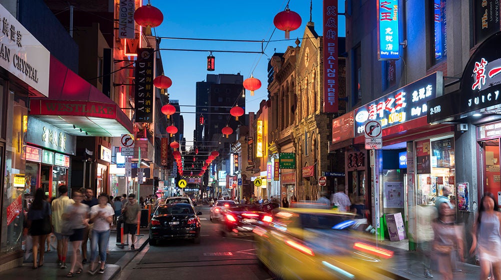 Taxi drives through Melbourne's busy Chinatown, Little Bourke Street, at dusk.