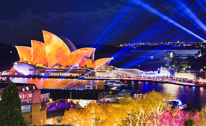 Generic modern architecture of Sydney CBD cityscape during Vivid Sydney light show brightly illuminated on buildings around harbour with blue beams in the sky.