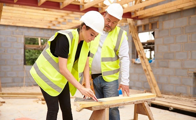Carpenter With Female Apprentice Working On Building Site