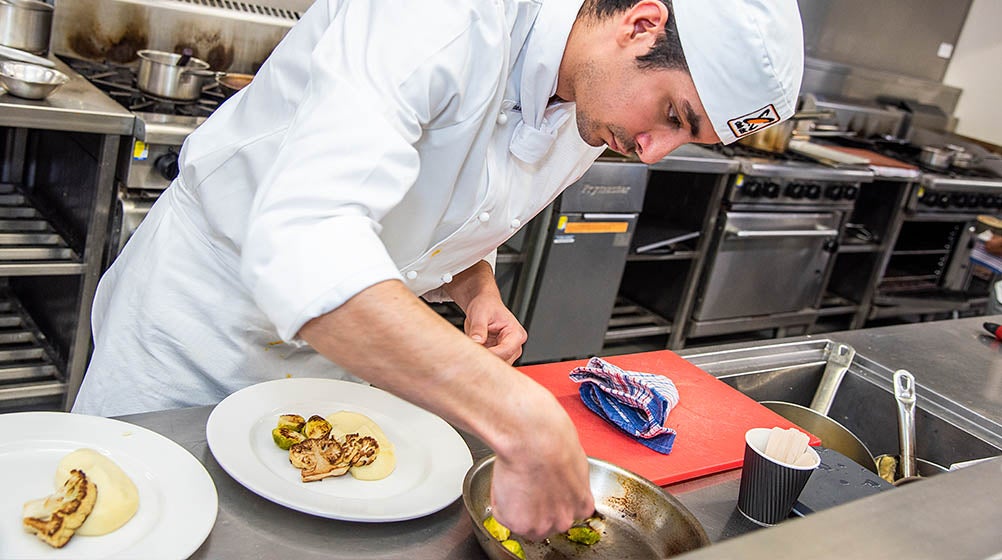 Holmesglen student carrying two dishes of food to a customer at the Holmesglen facility.