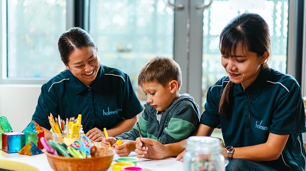 Image of a child with two Holmesglen students sitting in the childcare teaching facility.