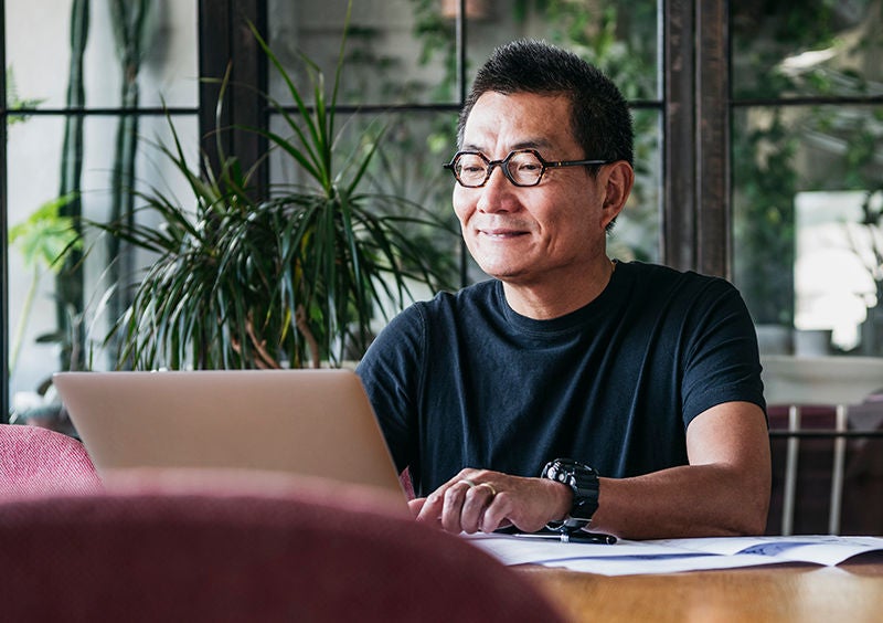 Mature man in glasses at home, typing on computer, contented, small business owner