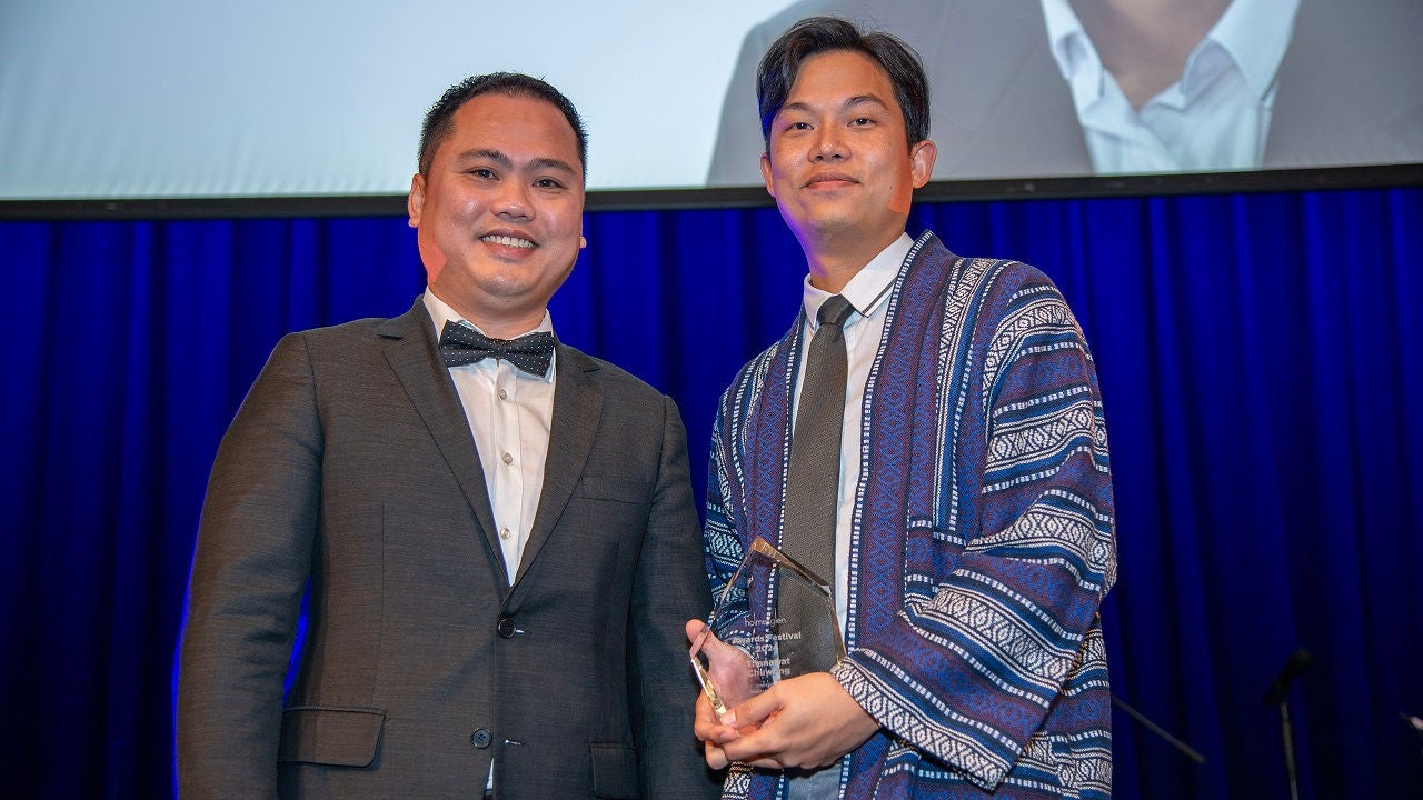 Student Thanawat Chuwong receives award on stage, as he smiles to the camera.