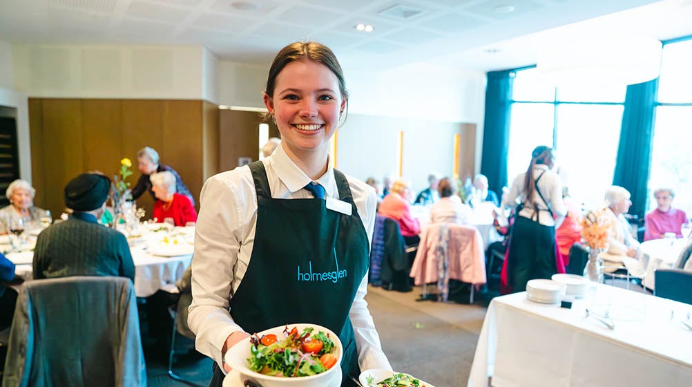 Holmesglen student carrying two dishes of food to a customer at the Holmesglen facility.
