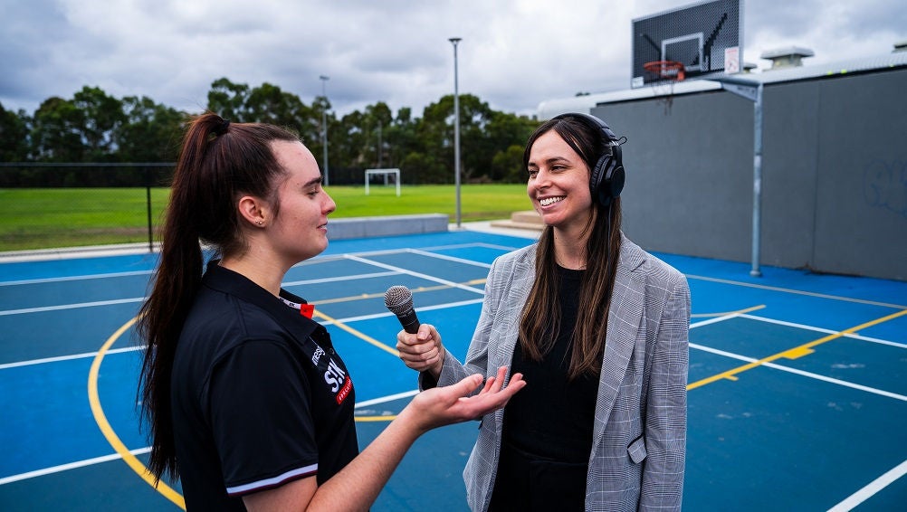 Sports learner with microphone interviews student athlete.