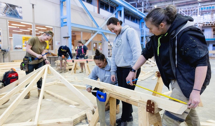 Four female apprentices work on a carpentry frame together in a trades' training workshop.