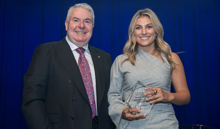 Female award winner stands on stage and receives trophy from Board member.
