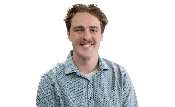 Male student wearing a collared shirt smiles to the camera, with a white background.