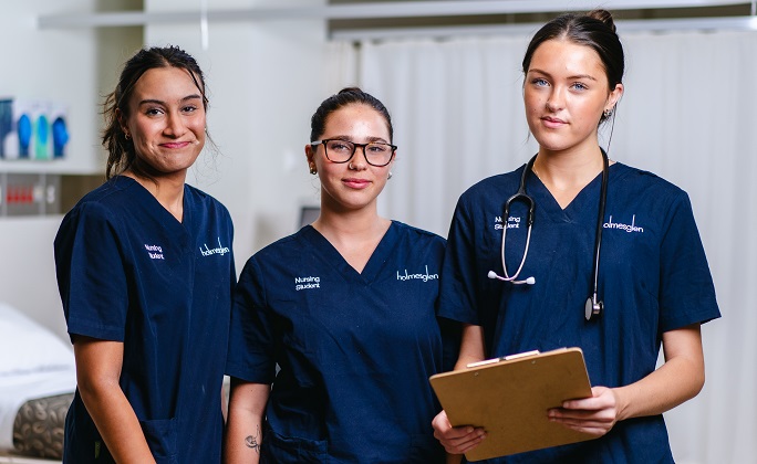 Three nursing students stand in a simulated training ward during class.