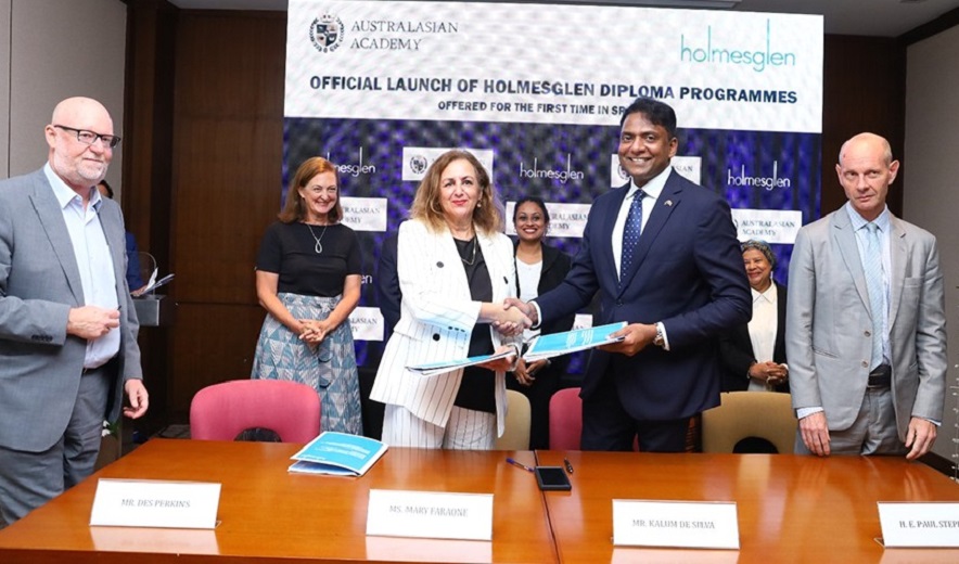 Four individuals stand behind a table, with the two middle individuals shaking hands after signing a partnership agreement.