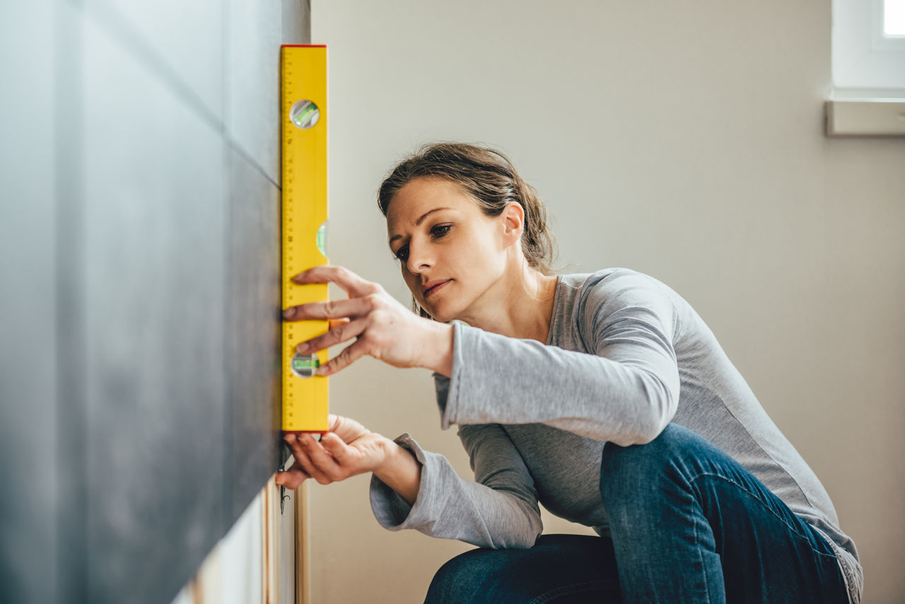 Woman wearing grey shirt using leveling tool at home