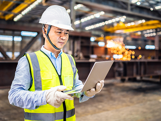 Asian engineer using a laptop in a factory.