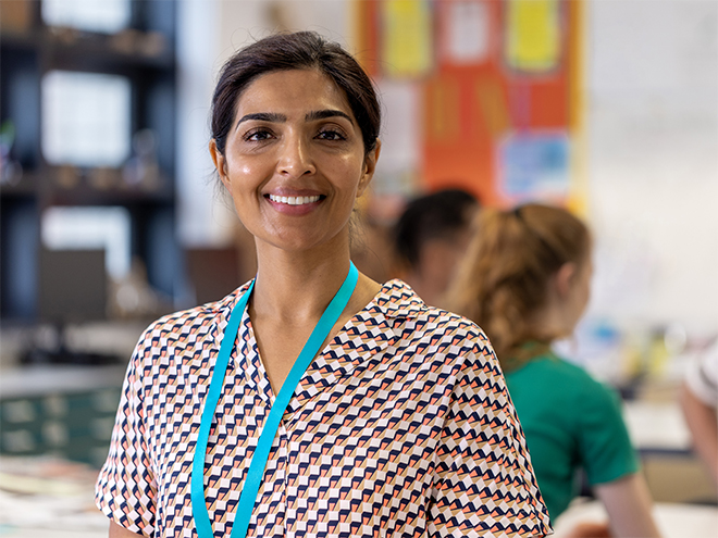 Teacher smiling looking at the camera while teaching an art class at a school in the North East of England. There are students out of focus behind her.