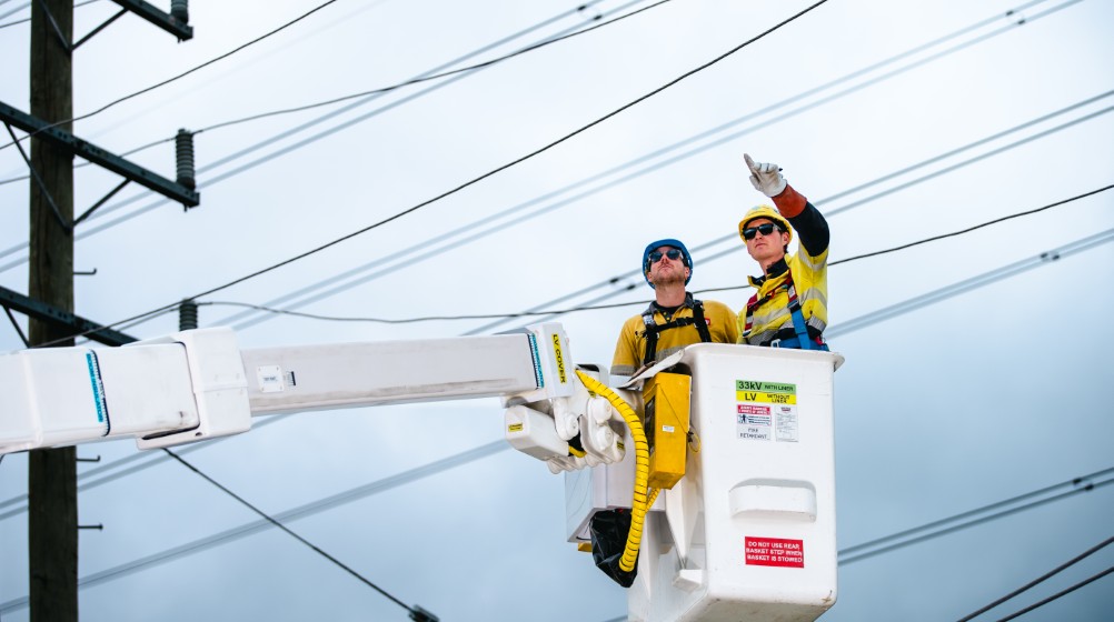 Two people in a crane working on an overhead powerline