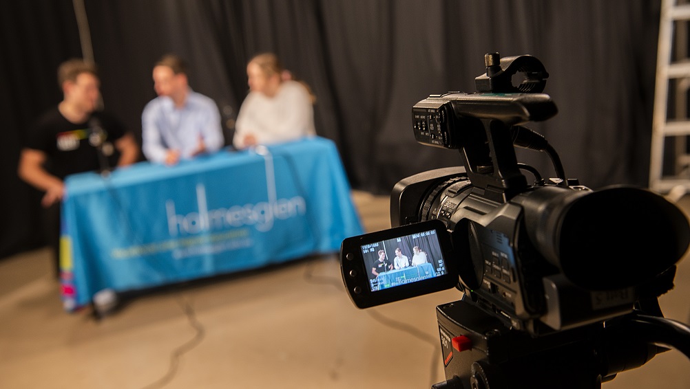 Three students sit in front of a camera for a student broadcast.