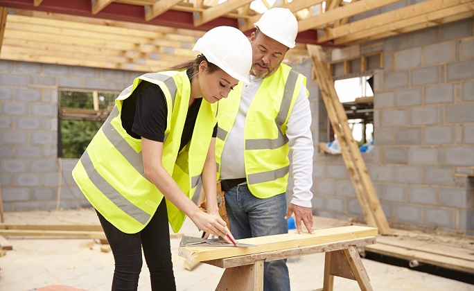 Carpenter With Female Apprentice Working On Building Site